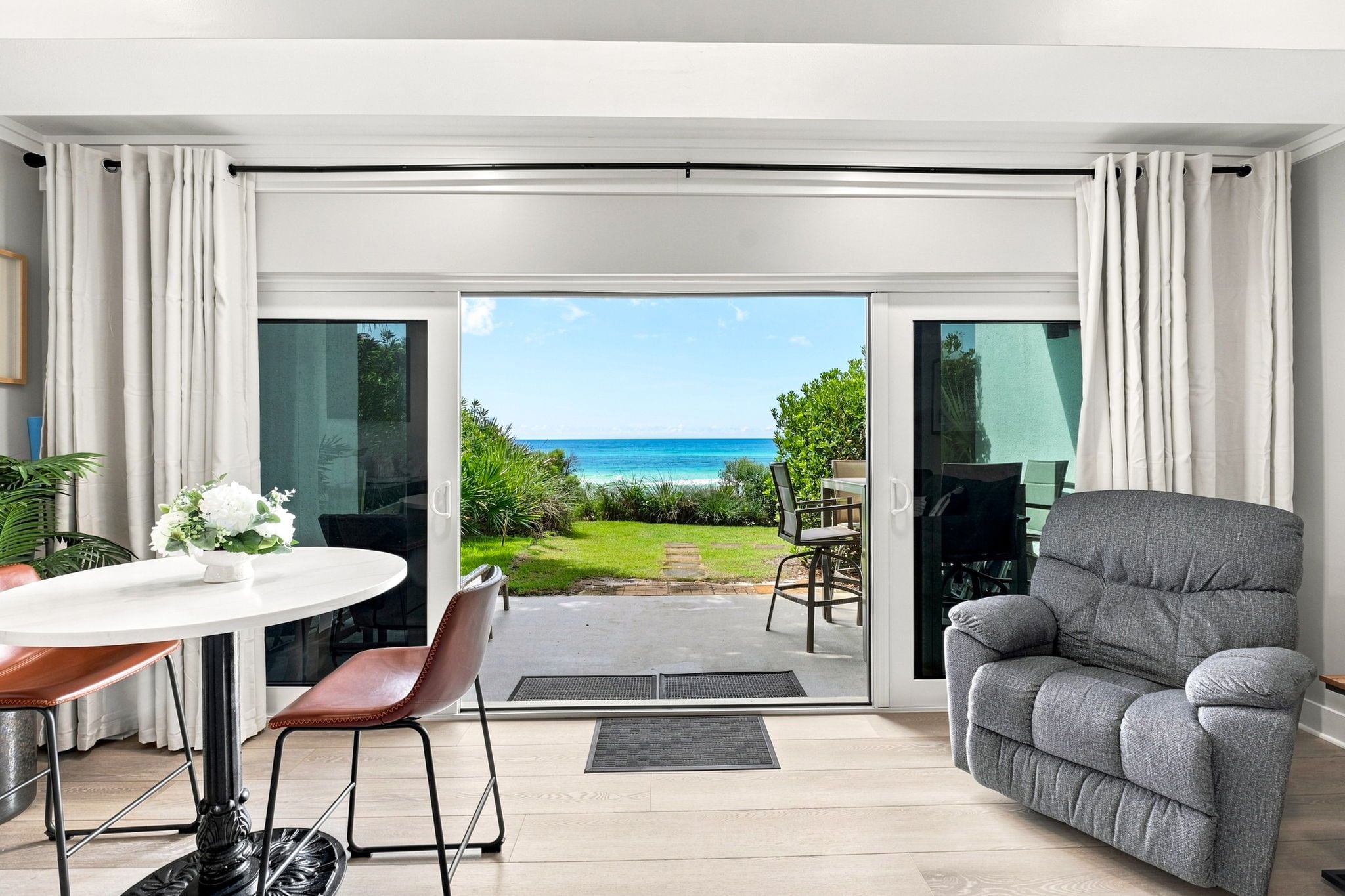 Ein modernes Wohnzimmer mit Meerblick, ein Essbereich mit Tisch und Stühlen sowie ein graues Sofa.