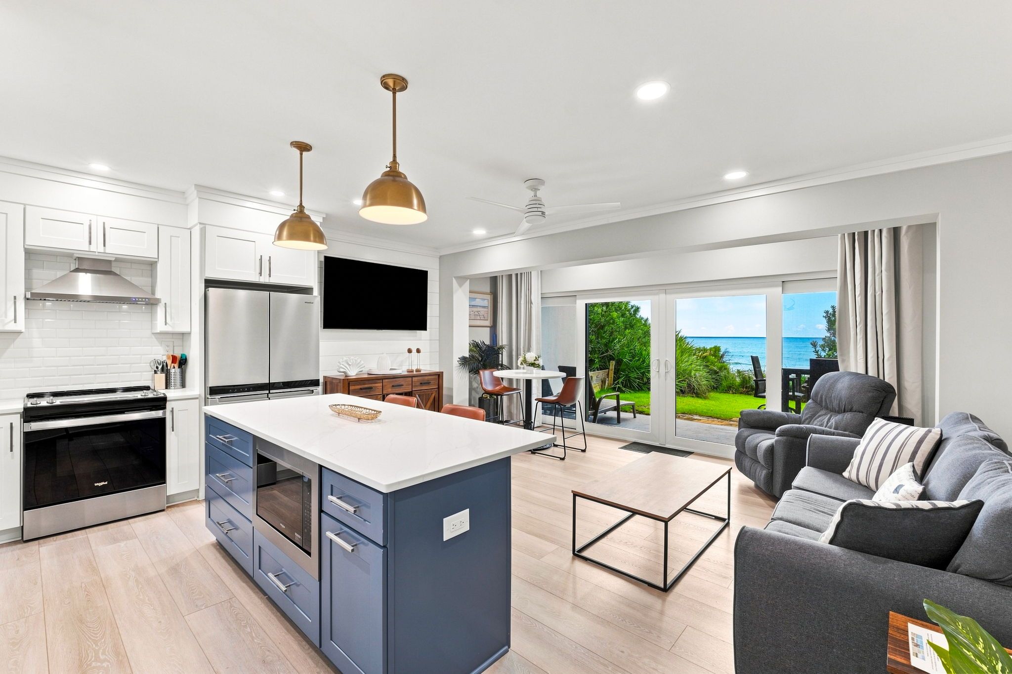 A modern kitchen with a central island, a dining area with a view, and a living room with a sofa and a coffee table.