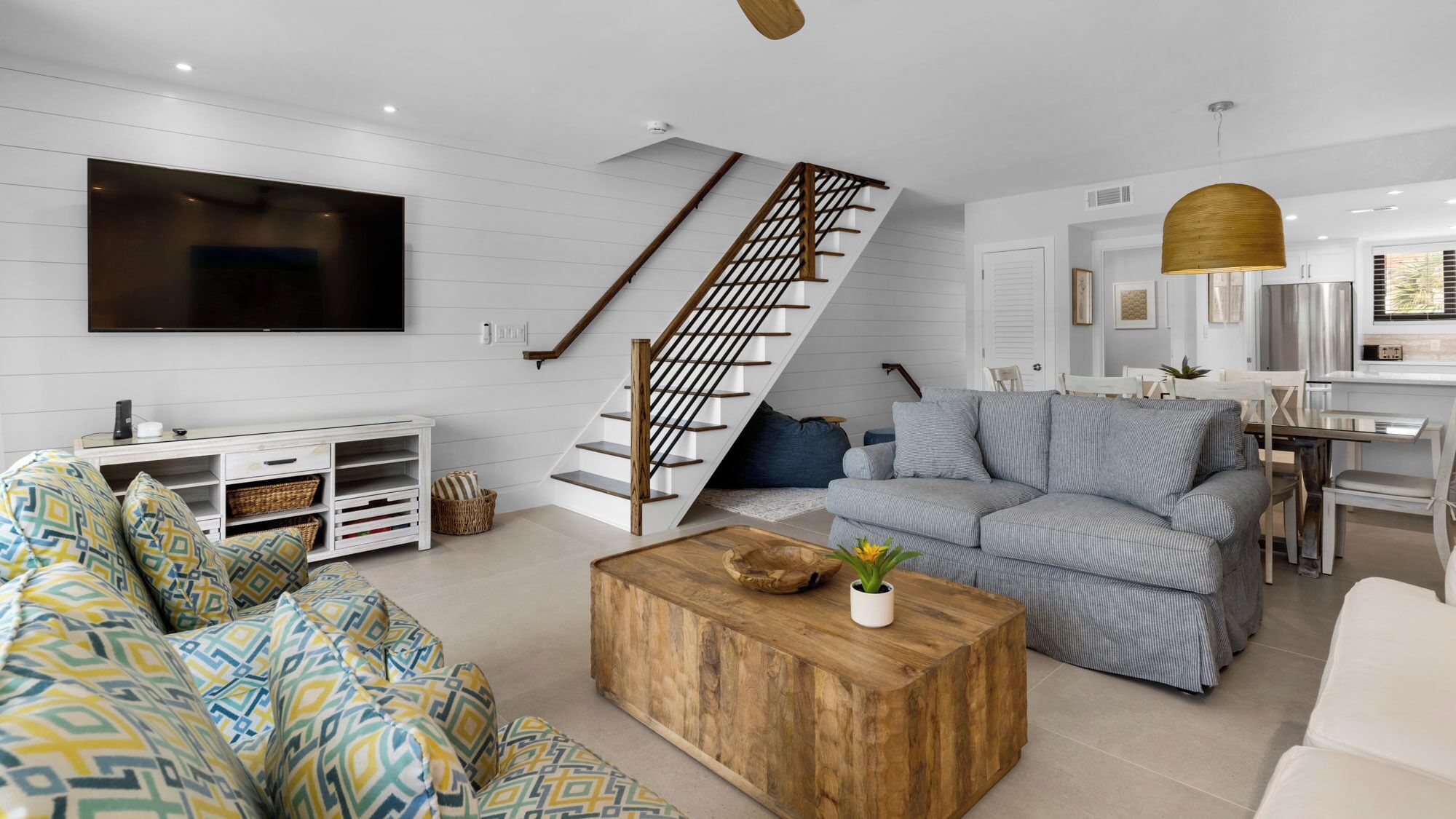 A modern living room with a staircase, a flat-screen TV, a wooden coffee table, and a dining area.