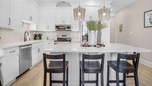A modern kitchen with white cabinetry, stainless steel appliances, and a central island with bar stools. -  Palms at Seagrove (Santa Rosa Beach)