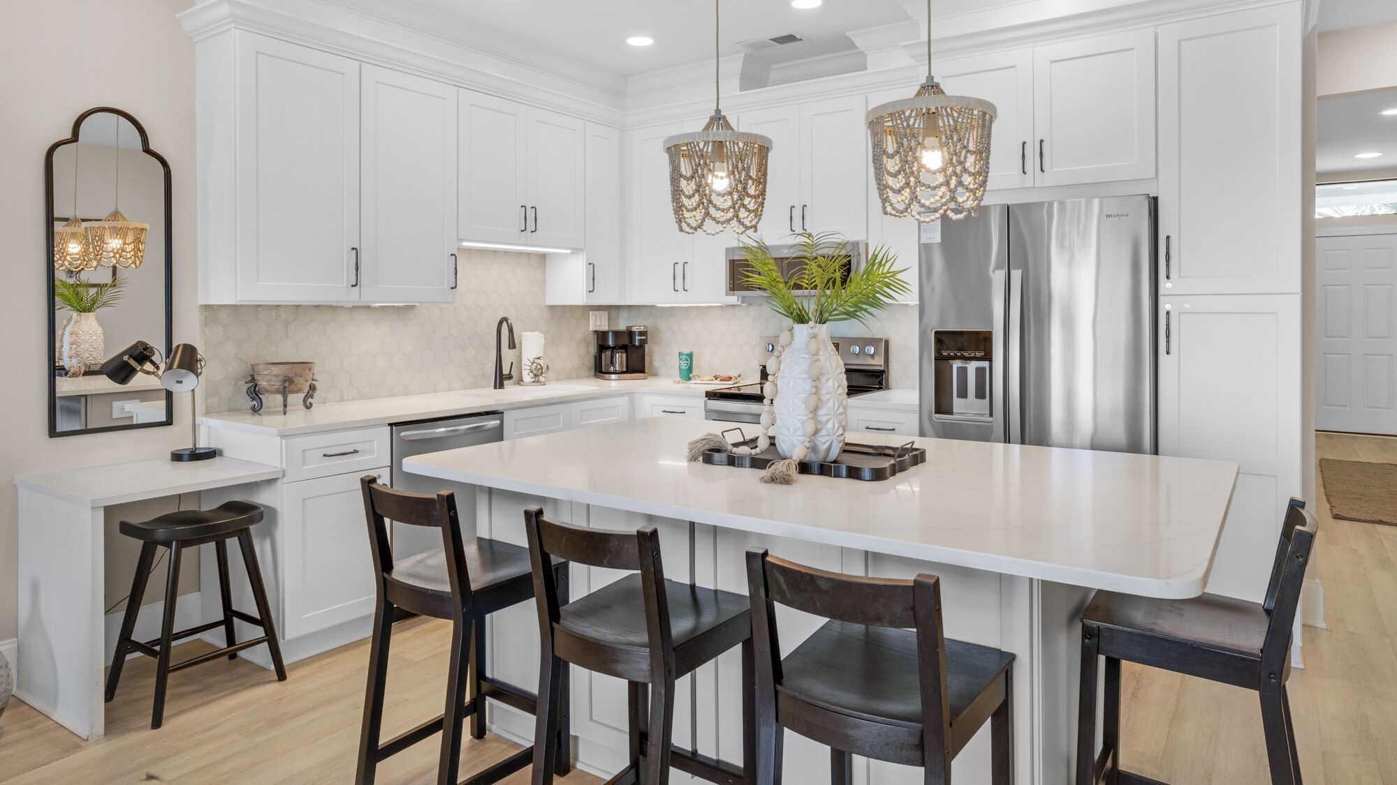 A modern kitchen with white cabinetry, a central island with bar stools, pendant lights, and stainless steel appliances.