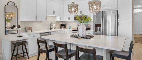 A modern kitchen with white cabinetry, a central island with bar stools, pendant lights, and stainless steel appliances.
