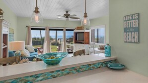 A spacious living area with a large window overlooking the ocean, a kitchen with a tiled backsplash, and a ceiling fan. -  Palms at Seagrove (Santa Rosa Beach)