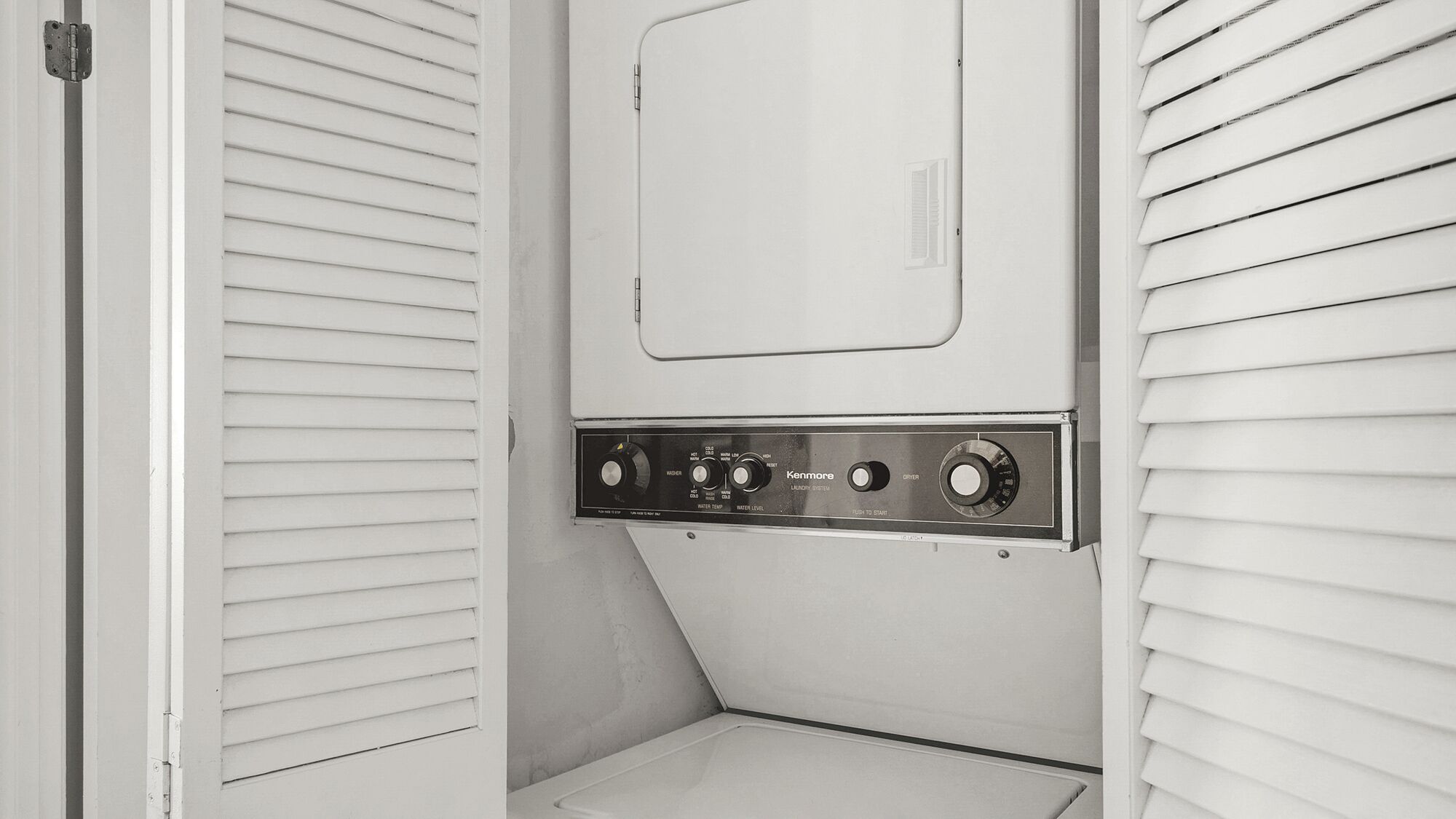 A compact, white laundry room with a Kenmore washer and dryer, featuring control knobs and a small window.