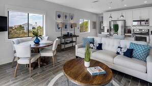 A modern living room with a dining area, kitchen, and large windows. -  Palms at Seagrove (Santa Rosa Beach)