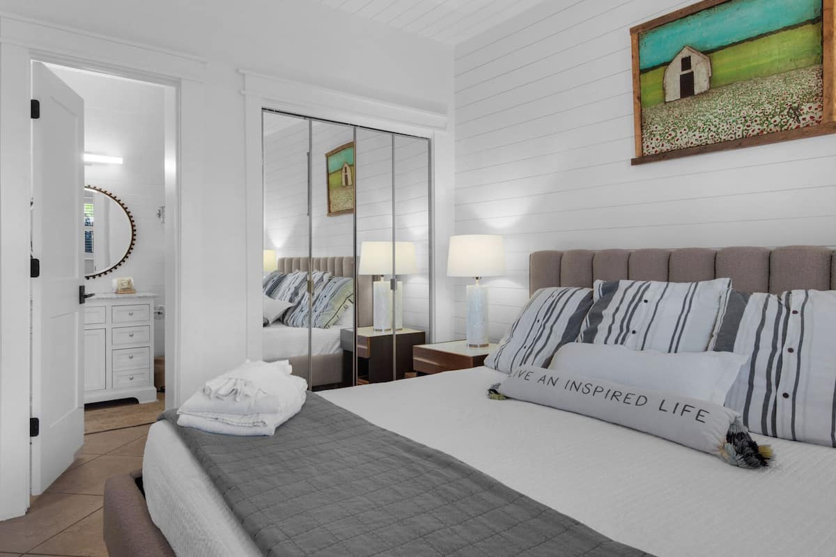 A hotel room with a bed, a bedside table, a mirror, a painting, and a wardrobe.