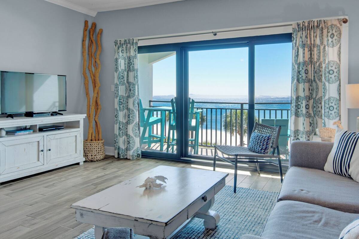 A living room with a TV, a sofa, a coffee table, and a balcony with a view of the sea.
