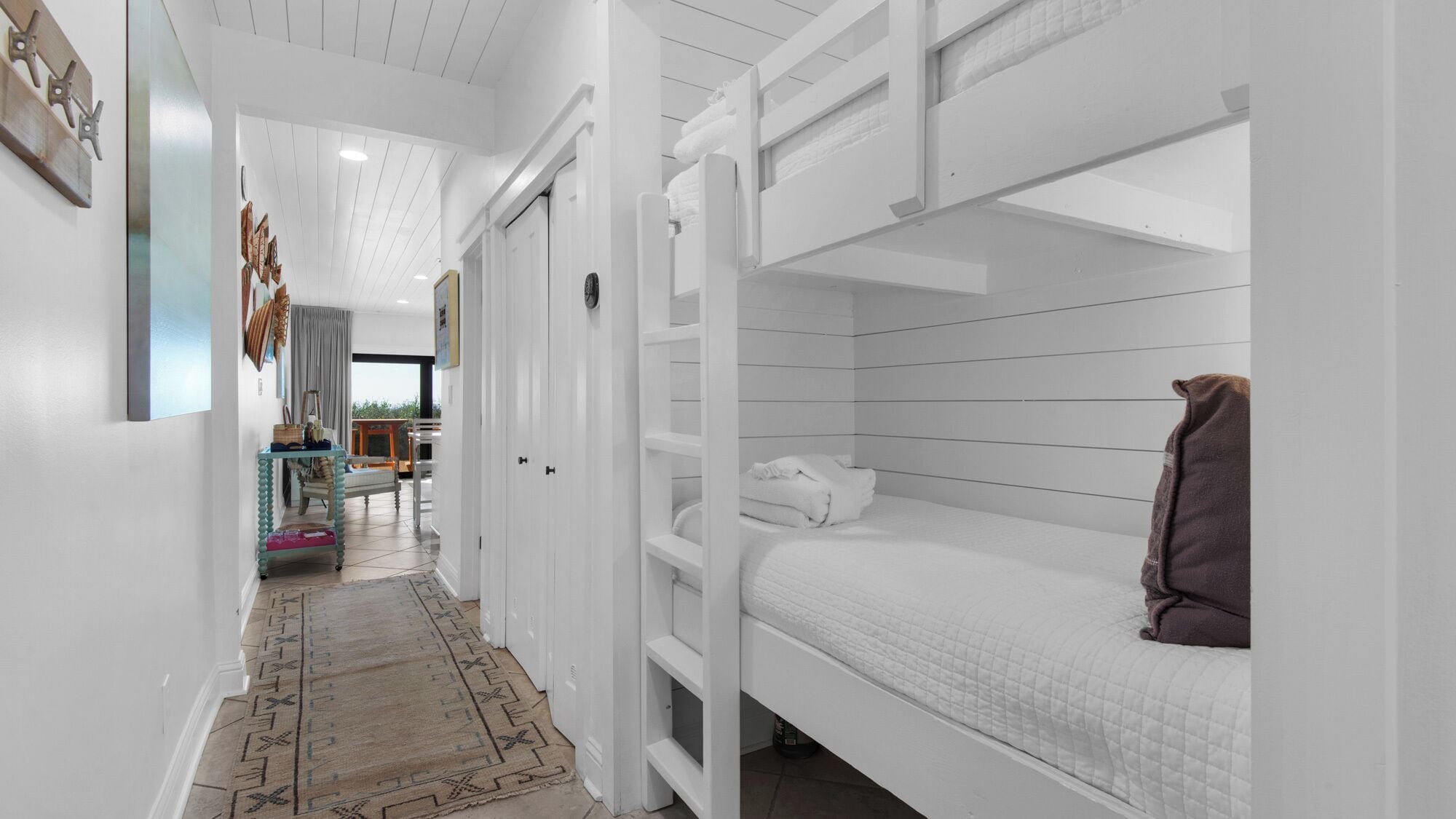 A narrow hallway with a bunk bed on the right, a small table with a chair, and a patterned rug.