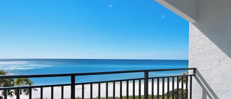 A balcony with a view of the ocean, a white wall, and a railing.