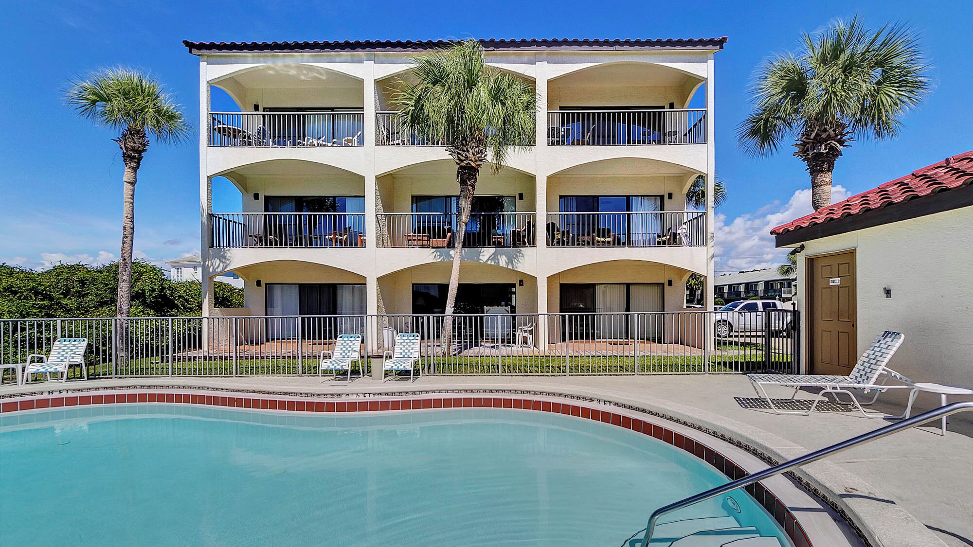 A multi-story hotel with a pool, balconies, and palm trees.