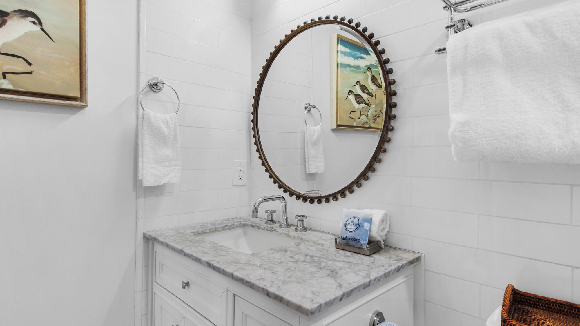 Une salle de bain avec un lavabo en marbre, un miroir rond doté d’un cadre décoratif et un porte-serviettes.