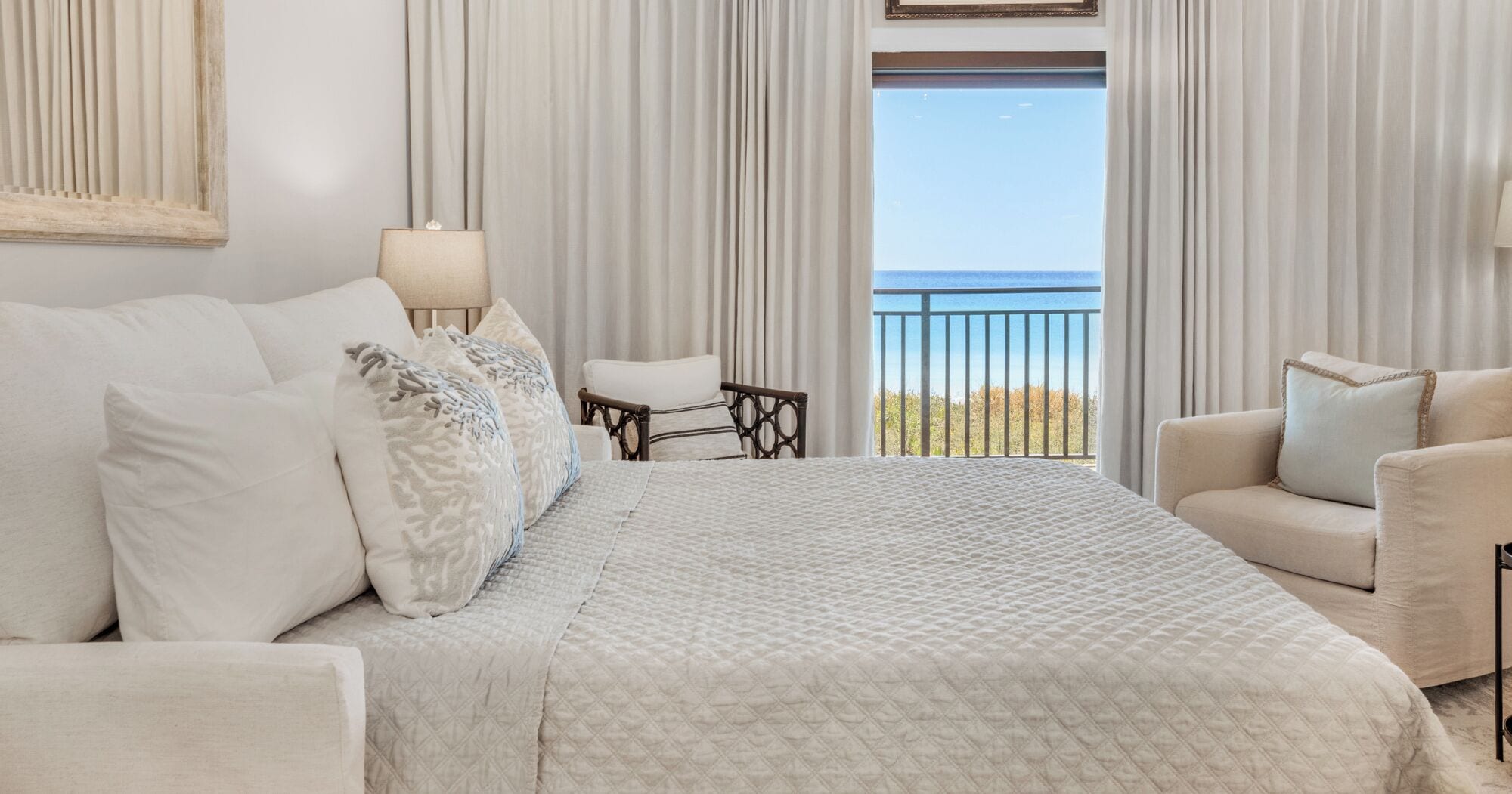 A hotel room with a large bed, a chair, a small table, and a view of the ocean.