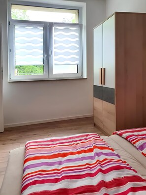 A bedroom with a bed, a wardrobe, and a window with a view of greenery.