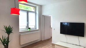 A room with a large window, a flat-screen TV mounted on the wall, a radiator below the window, and a potted plant. - Apartment 'Geräumige Moderne 3 Raumwohnung' with Shared Terrace and Wi-Fi (Dohna)