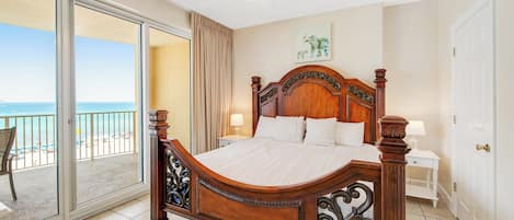 A bedroom with a large bed, a ceiling fan, a view of the beach, and a sliding glass door to the balcony.