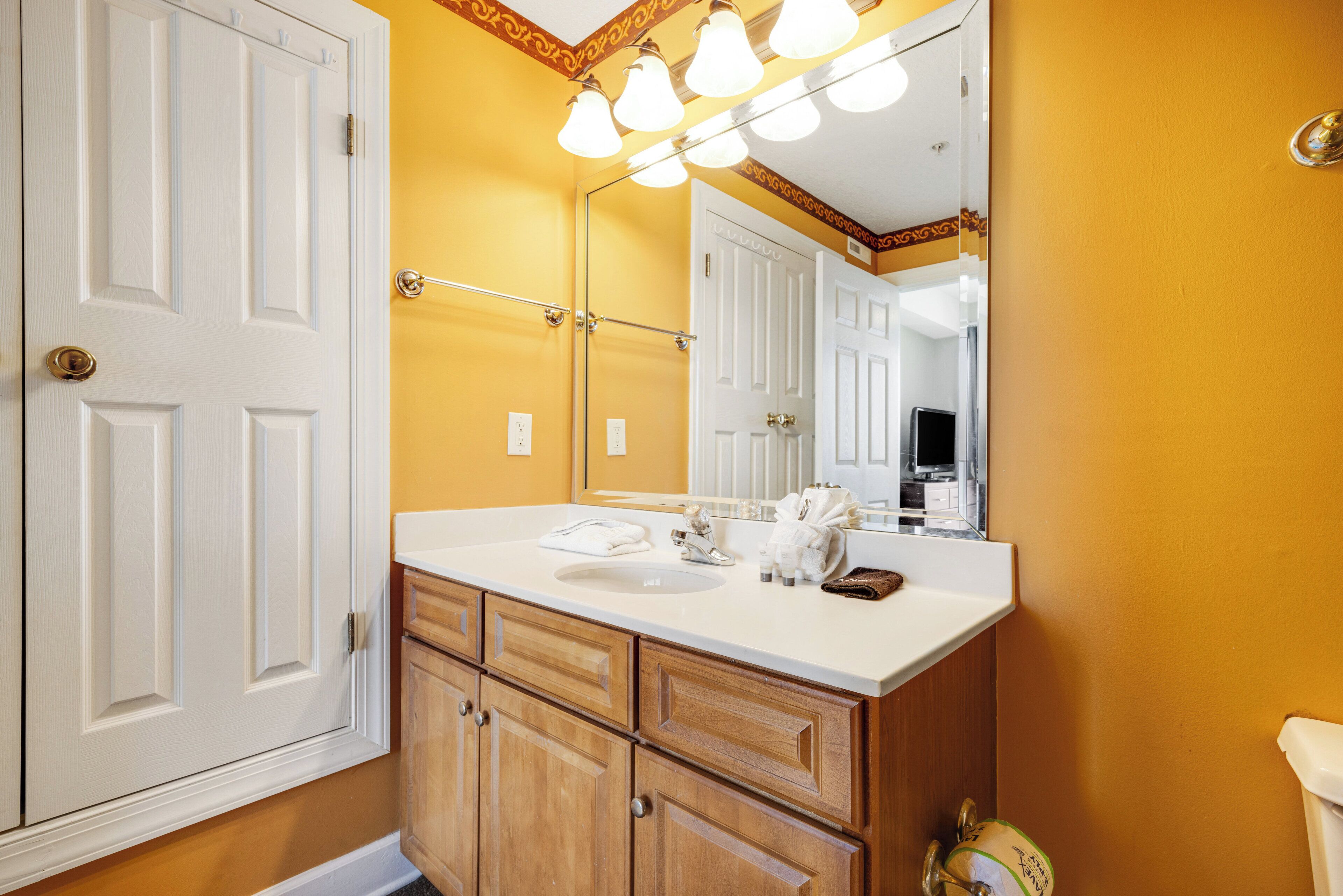 A bathroom with a white vanity, wooden cabinets, a mirror, and a towel rack.