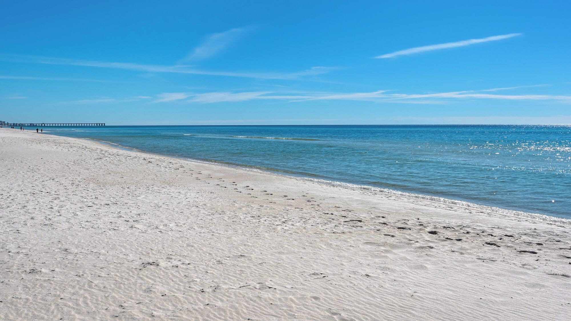 Une plage avec une jetée visible au loin.