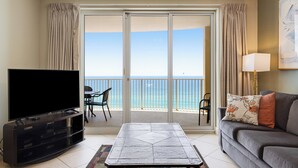 Ein Wohnzimmer mit Flachbildfernseher, grauem Sofa, Couchtisch und Balkon mit Meerblick.