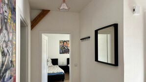 Un pasillo que conduce a un dormitorio con cama, mesita de noche, espejo y lámpara en el techo.