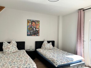 A bedroom with two beds, a nightstand, a lamp, a painting on the wall, and a window with curtains. - Apartment 'Frisch Freche 3 R' with Private Terrace and Wi-Fi (Dohna)