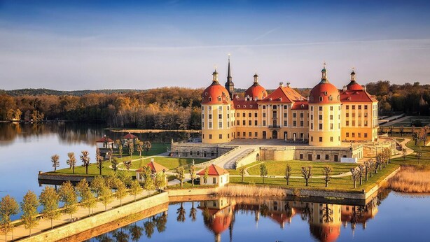 Un edificio grande e histórico con múltiples cúpulas, un patio central y un lago al frente.