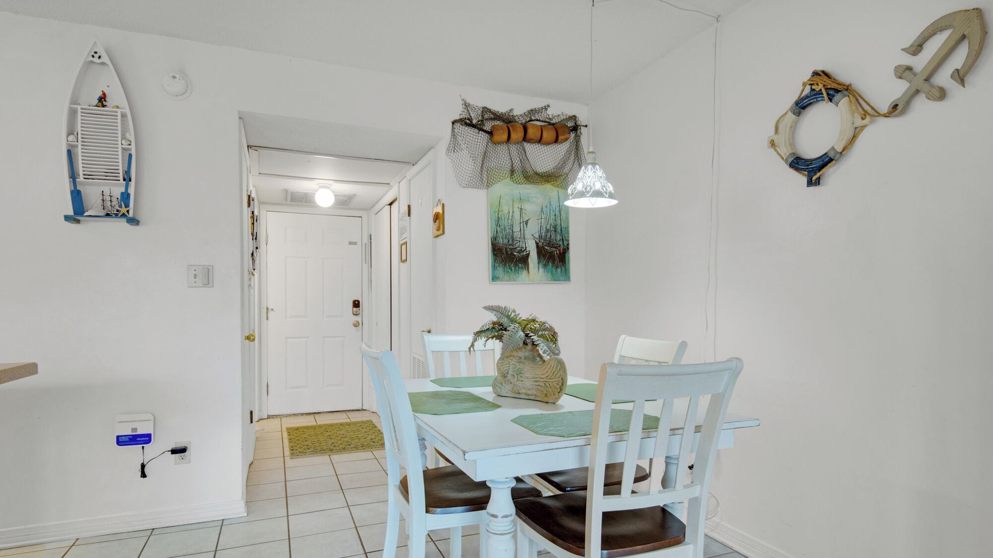 A dining area with a white table and chairs, a decorative plant, and nautical-themed wall decor.