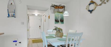 A dining area with a white table and chairs, a decorative plant, and nautical-themed wall decor.