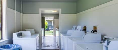A laundry facility with multiple washing machines and dryers, a blue trash bin, and a concrete floor.