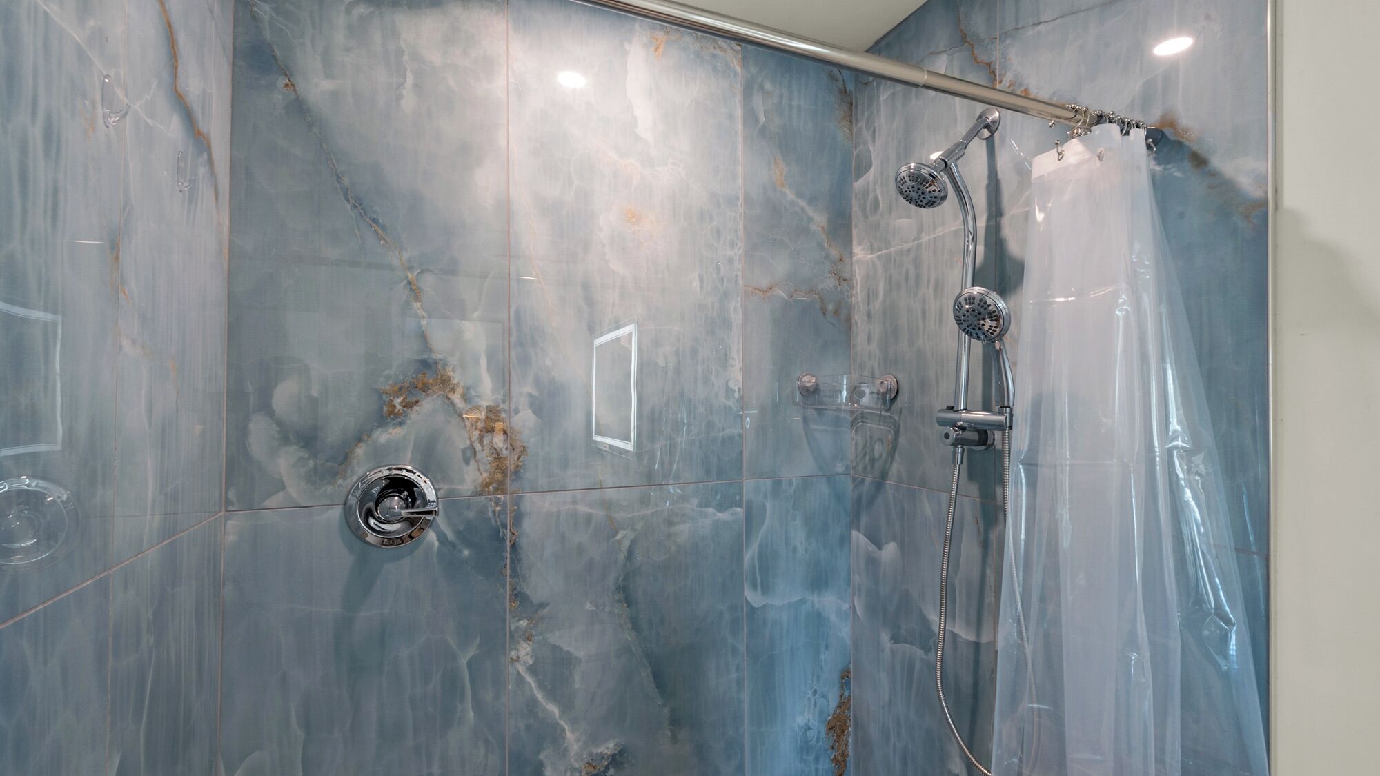Ducha con cabezal de ducha de mano y cabezal de ducha de lluvia empotrado en la pared, ambos con acabados cromados.