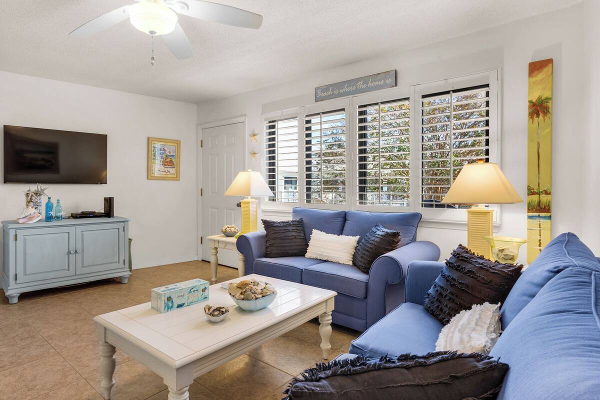 A living room with a blue sofa, a white coffee table, and a television on the wall.