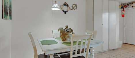 A dining area with a white table, green placemats, and a decorative vase. There are two hanging lamps and a white wardrobe in the background.
