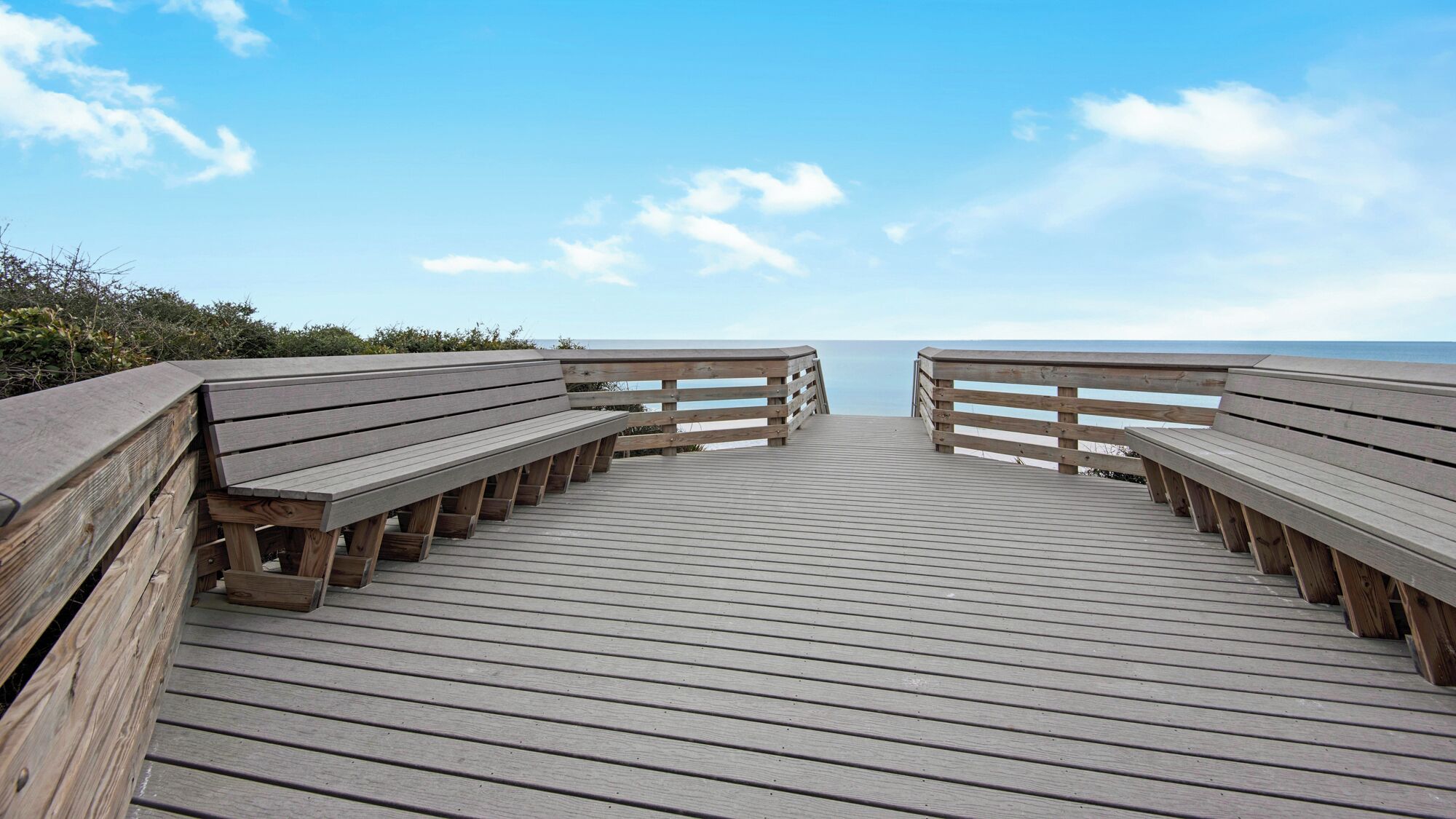 A wooden boardwalk leading to a beach with benches on both sides.