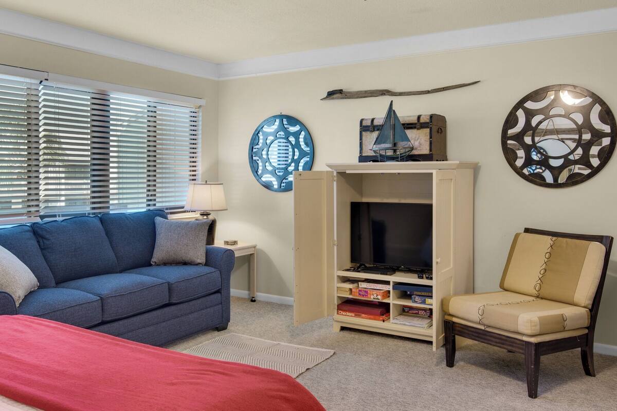 A living room with a blue sofa, a red blanket, a beige armchair, a TV stand with a flat-screen TV, and decorative wall art.