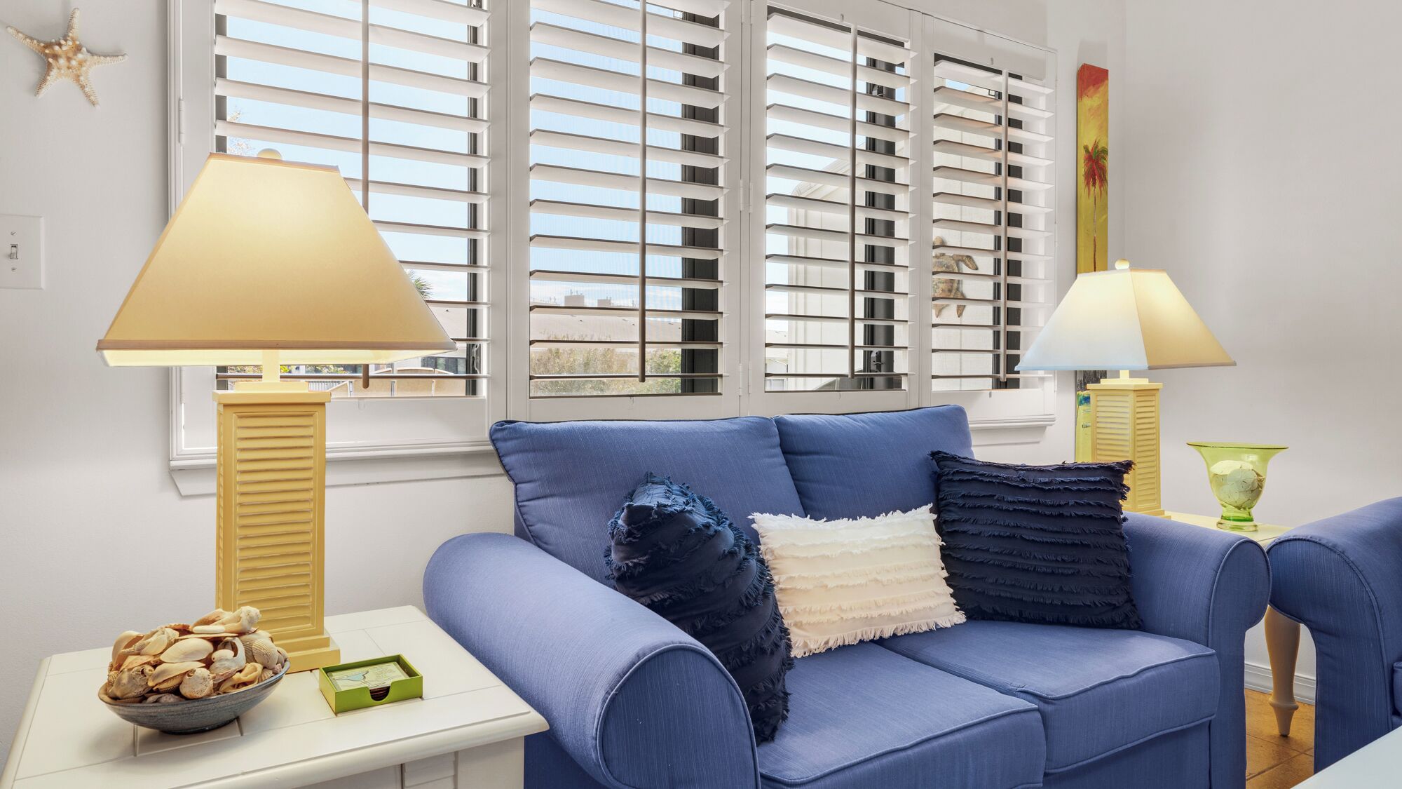 A living room with a blue sofa, two lamps, a starfish decoration, and a bowl of seashells on a side table.