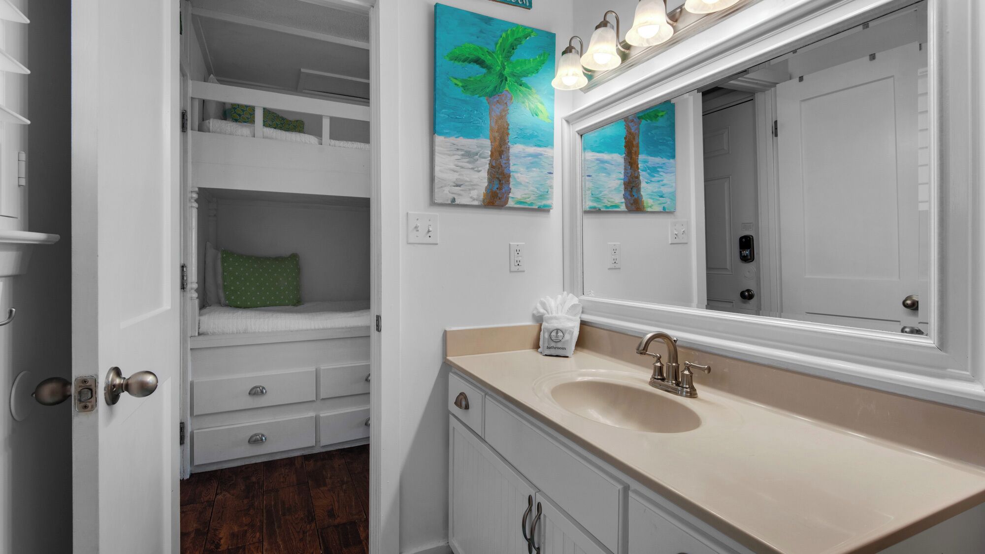 A compact bedroom with bunk beds, a bathroom with a sink and mirror, and artwork on the walls.