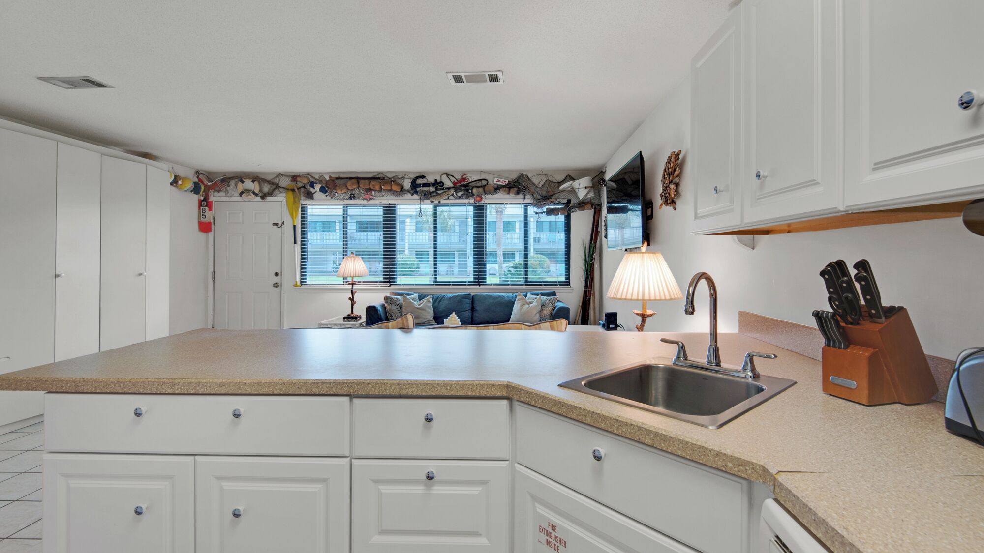 A kitchen with a large island, white cabinetry, a built-in sink, and a window with blinds.