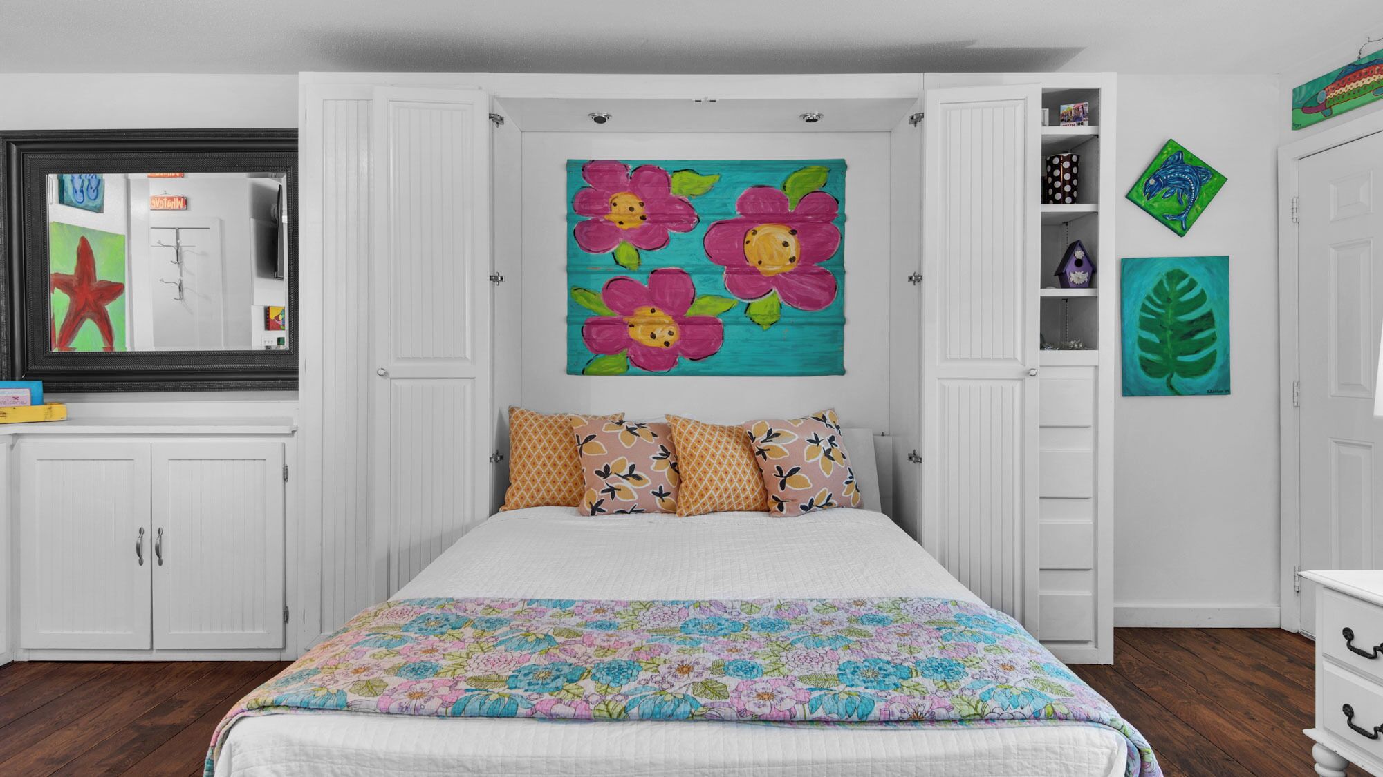 Une chambre à coucher avec un lit, une armoire blanche et un tableau floral aux couleurs vives accroché au mur.