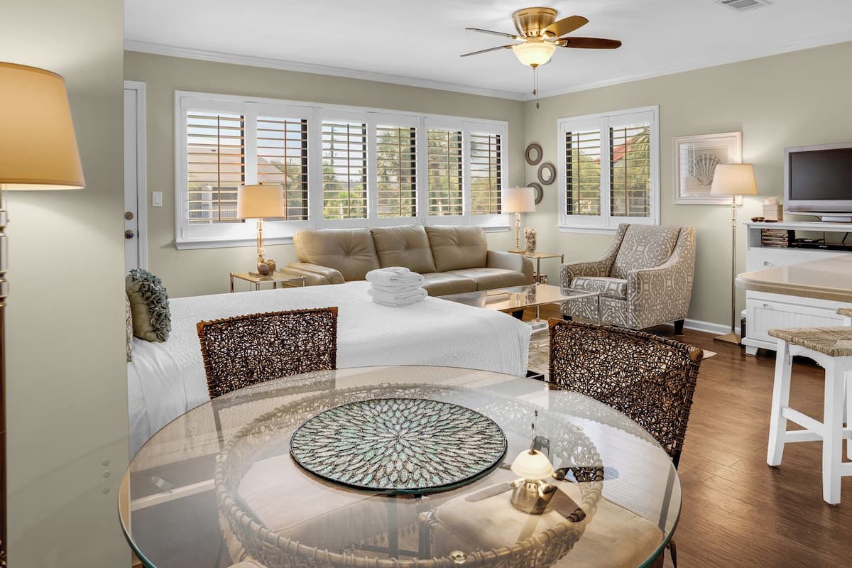A spacious living room with a round glass table, a sofa, a chair, and a television.