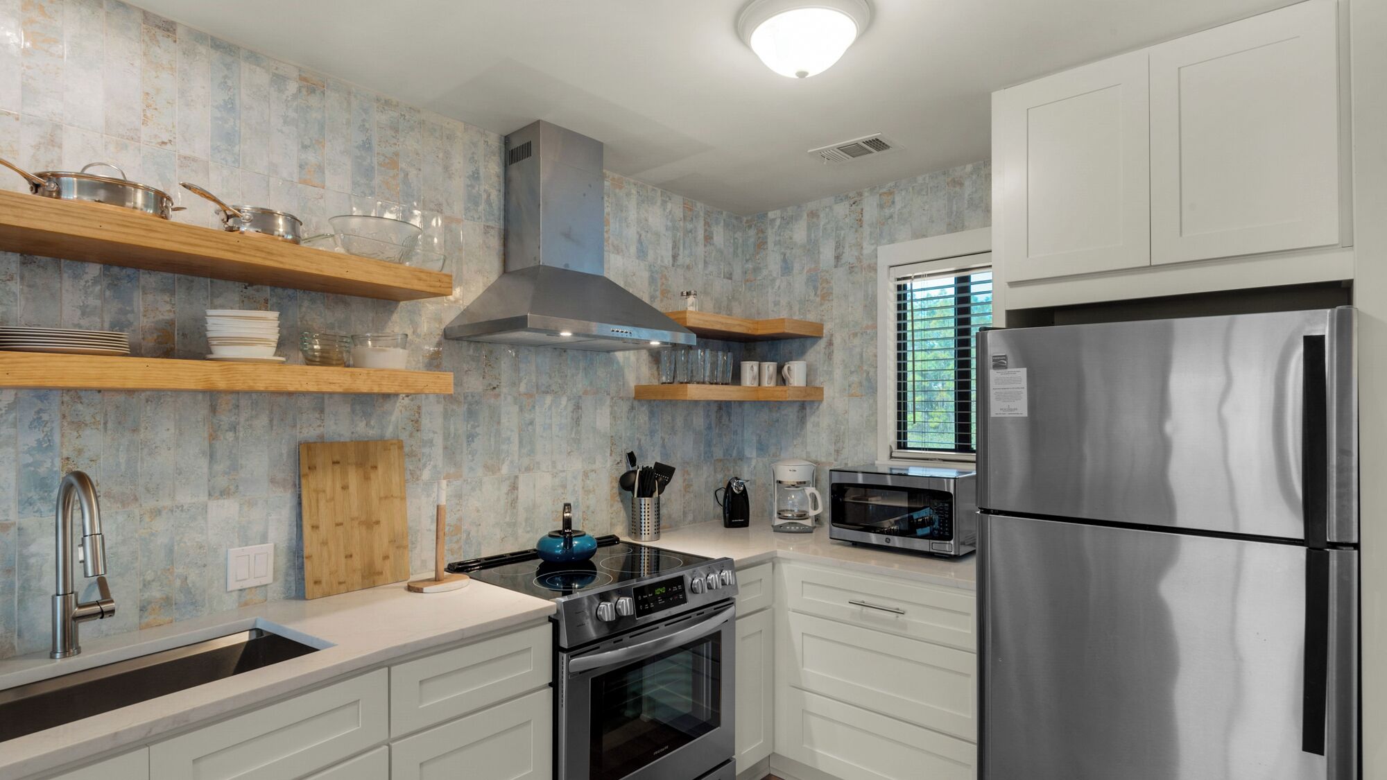 Una cocina moderna con armarios blancos, electrodomésticos de acero inoxidable y estantes de madera.