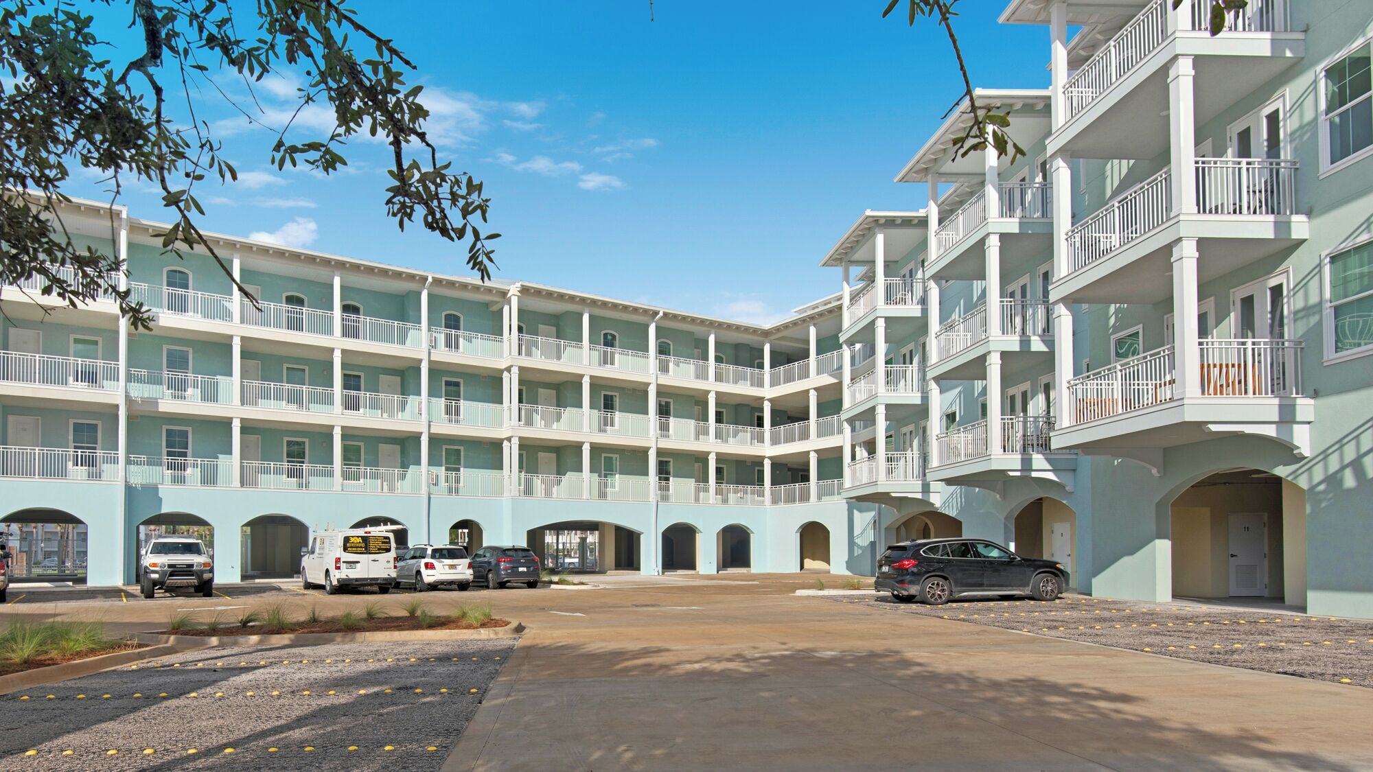 Un hotel su più piani con un cortile centrale, caratterizzato da balconi su ogni piano, un'area di parcheggio con diversi veicoli e un cielo azzurro intenso.