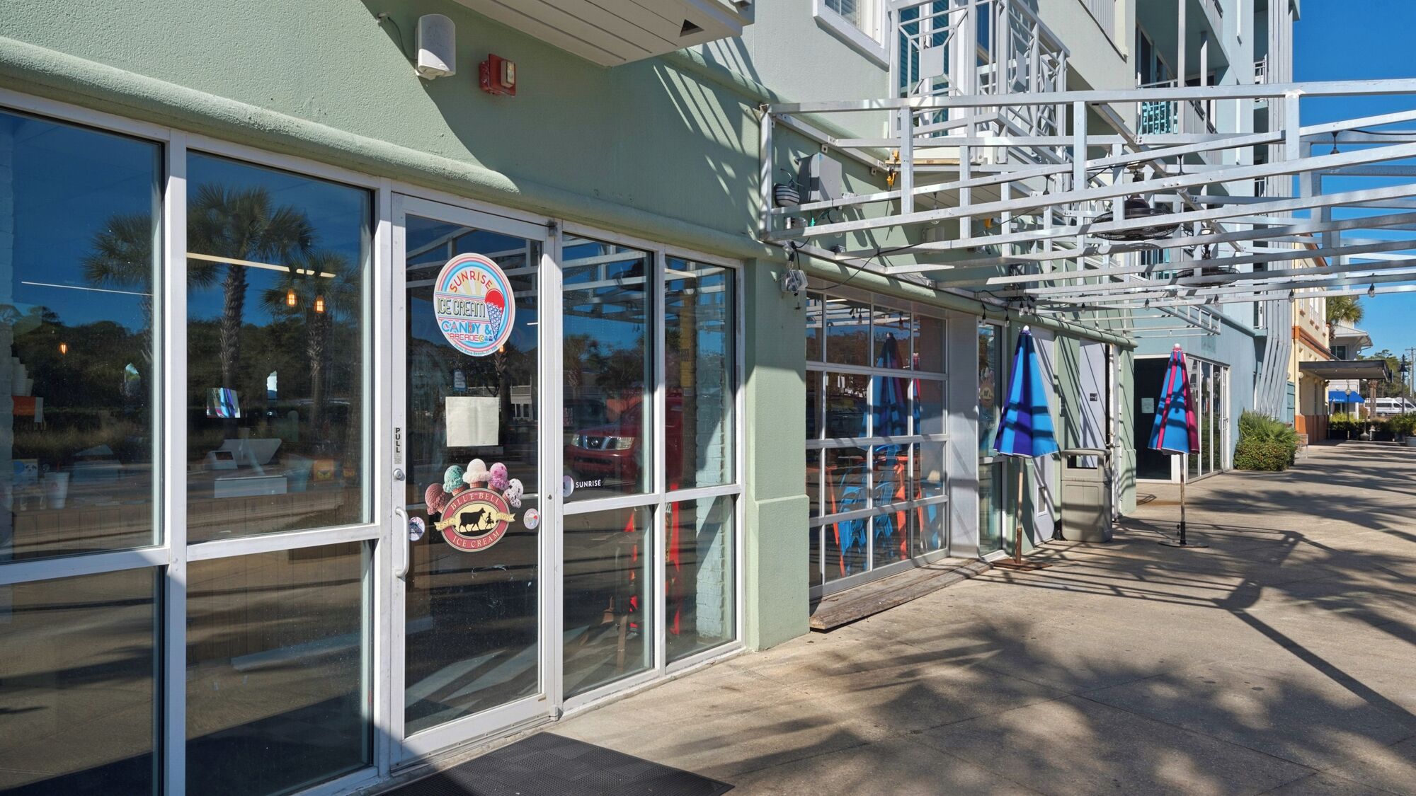 Une devanture de magasin avec de grandes vitrines, une enseigne indiquant « Sunrise Ice Cream », et un parasol bleu à l’extérieur.