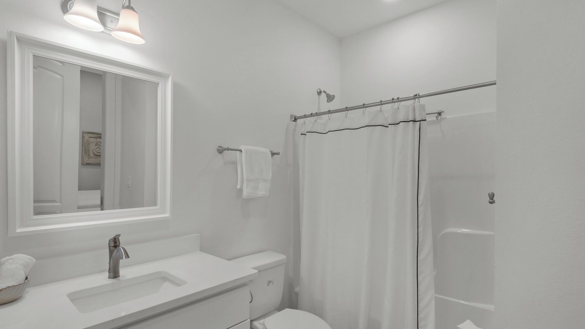 Ein Badezimmer mit einem weißen Waschbecken, einem Spiegel und einer Toilette. Ein Duschvorhang und ein Handtuchhalter sind vorhanden.