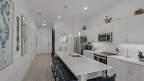 Una cocina moderna con armarios blancos, un refrigerador de acero inoxidable, un microondas y una isla grande con taburetes de bar.