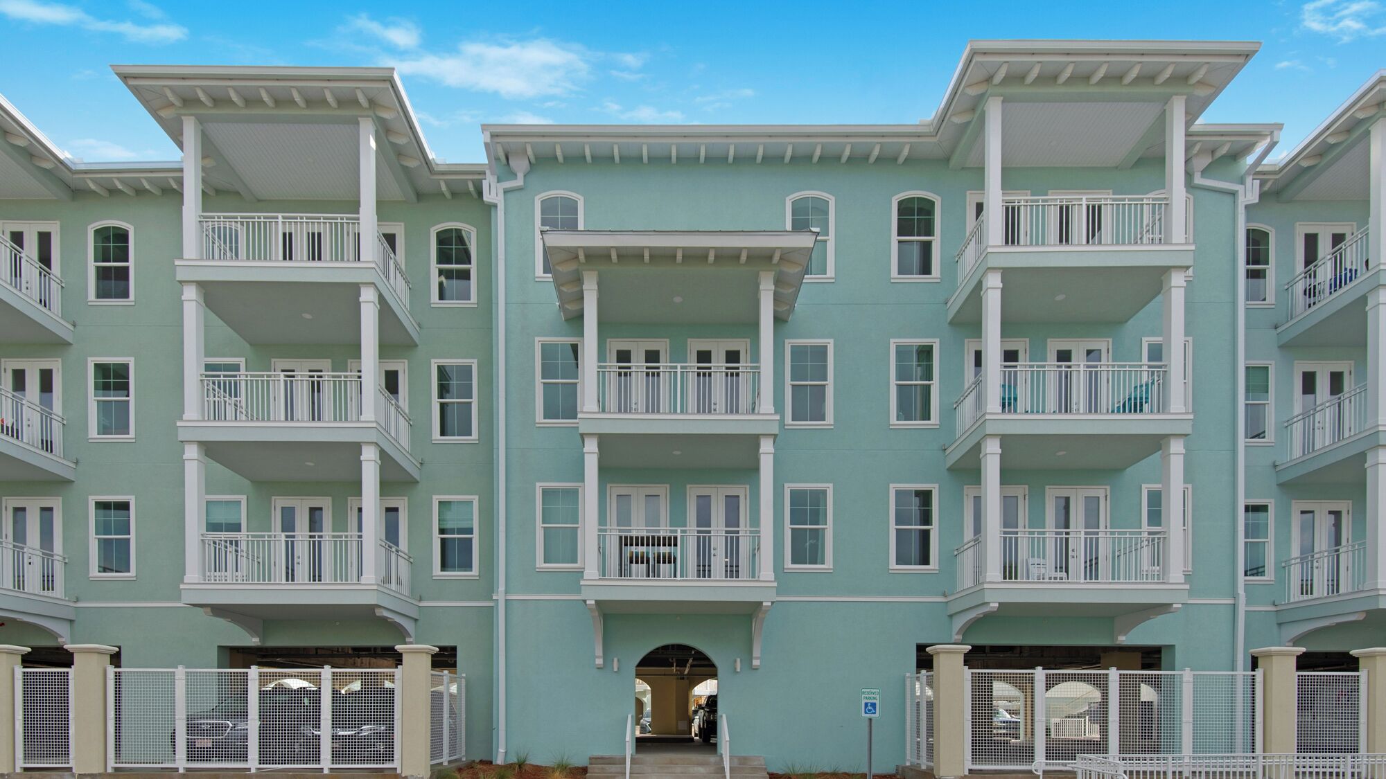 A multi-story residential building with balconies, a central entrance, and a parking area.