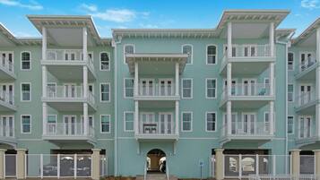 A multi-story residential building with balconies, a central entrance, and a parking area.