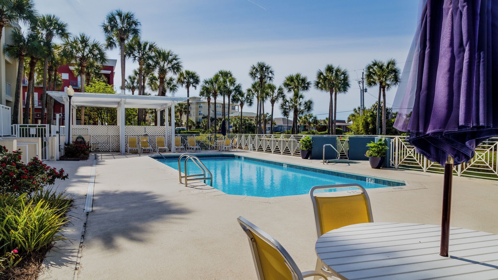 A pool area with a clear blue pool, yellow lounge chairs, and a covered seating area.
