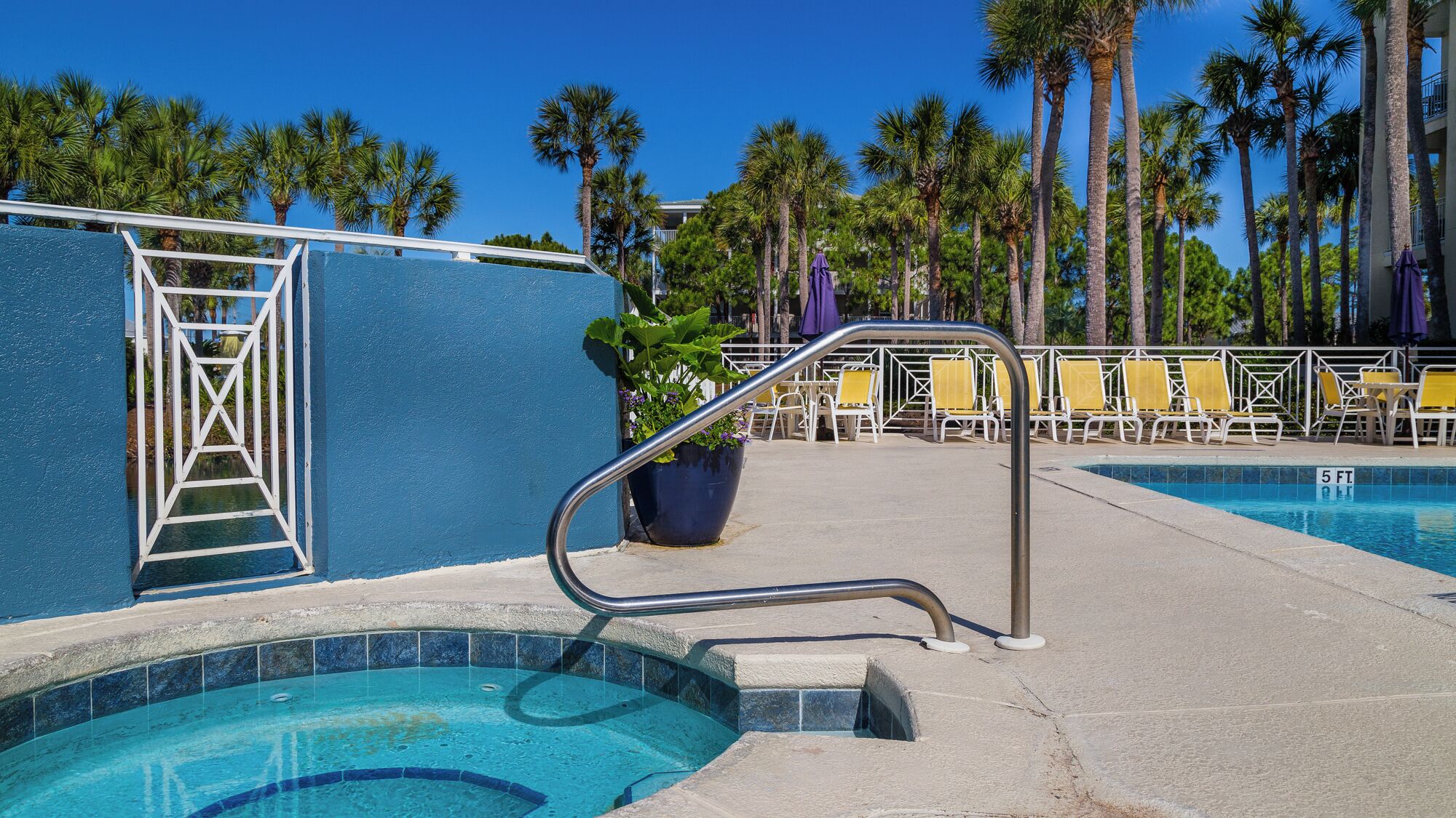 A pool area with a blue wall, a ladder, and yellow lounge chairs.
