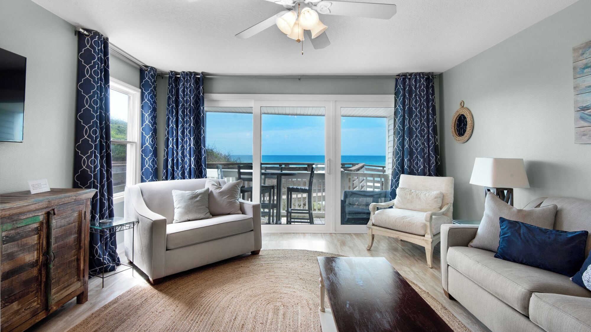 A spacious living room with a large sliding glass door leading to a balcony with a view of the ocean.