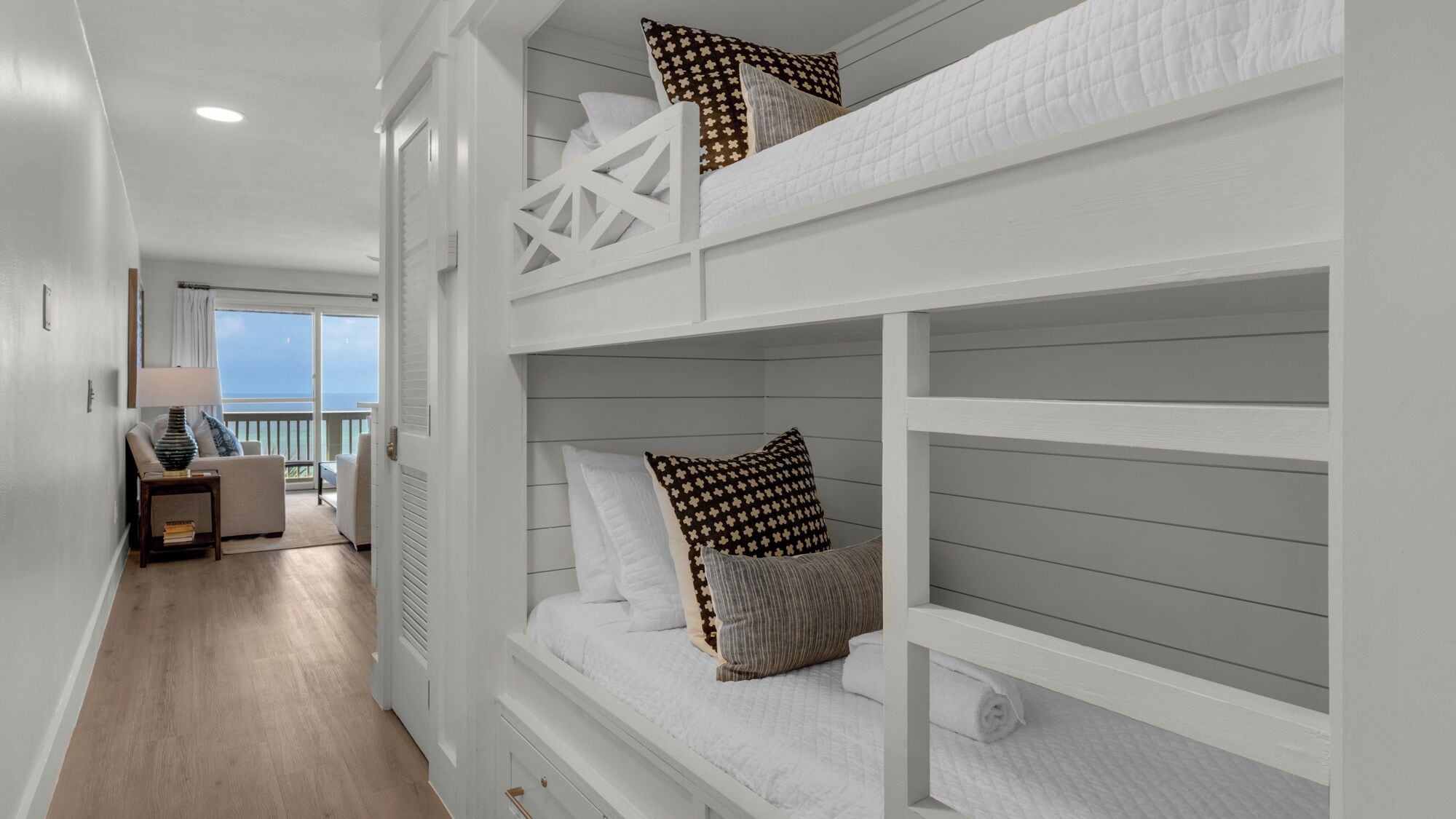 A bunk bed room with a view of the sea, a sofa, and a lamp.