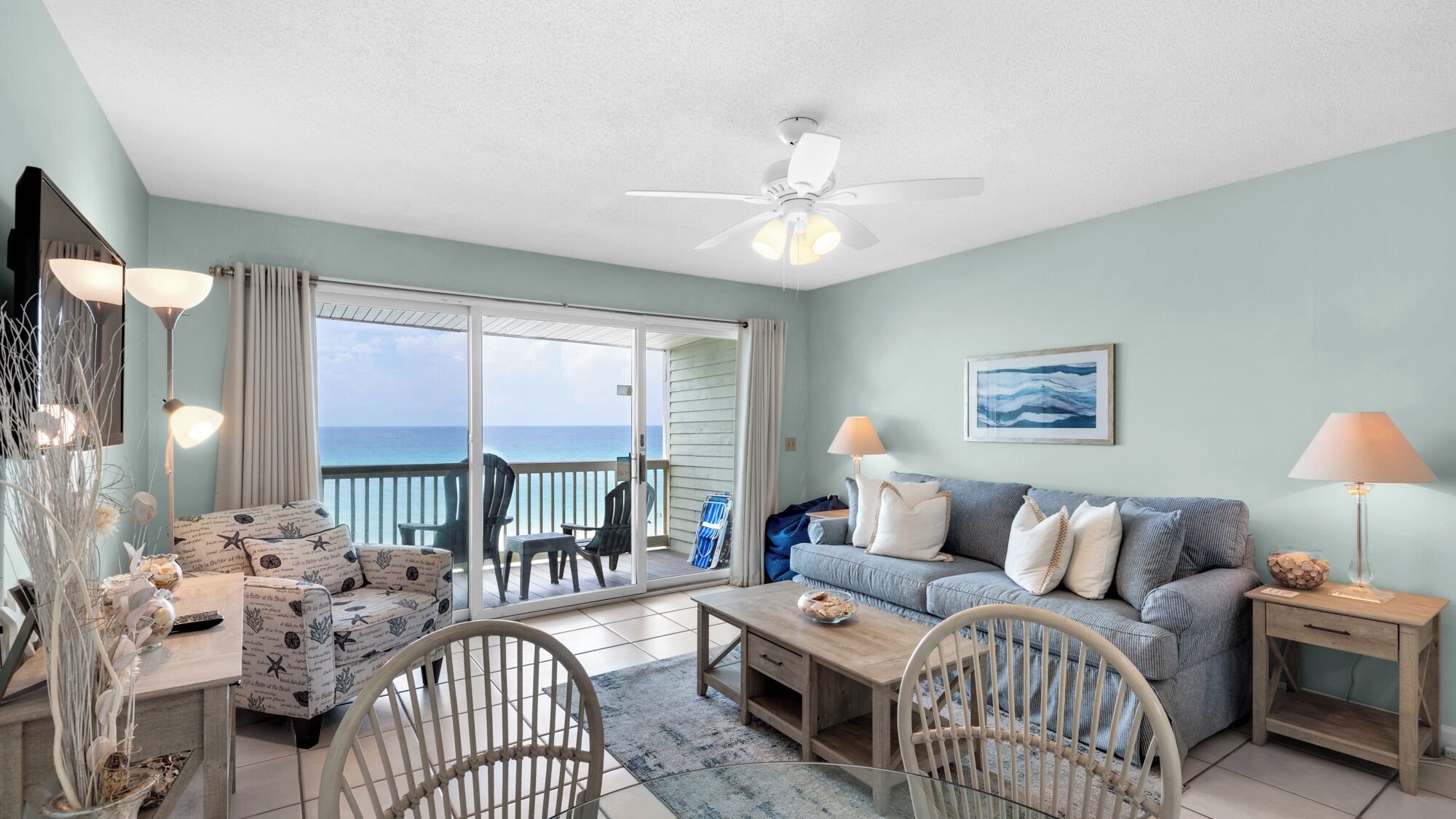 A spacious living room with a view of the ocean, a ceiling fan, and a dining area with a table and chairs.